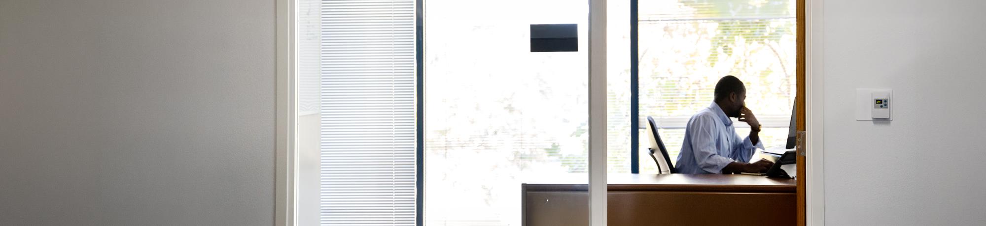 Silhouette of person using laptop in an office.
